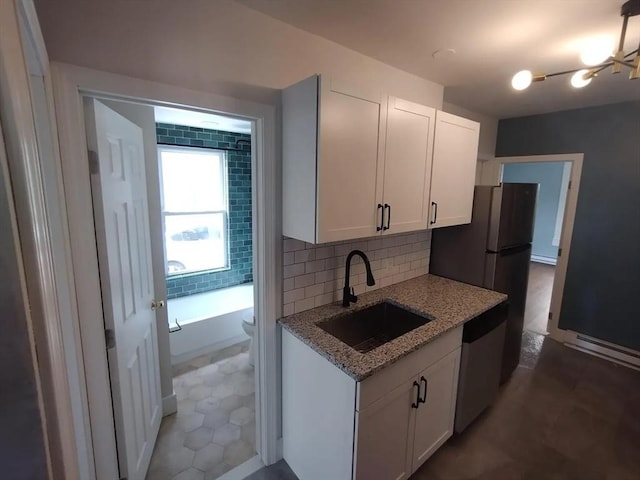 kitchen featuring appliances with stainless steel finishes, sink, white cabinets, decorative backsplash, and light stone countertops