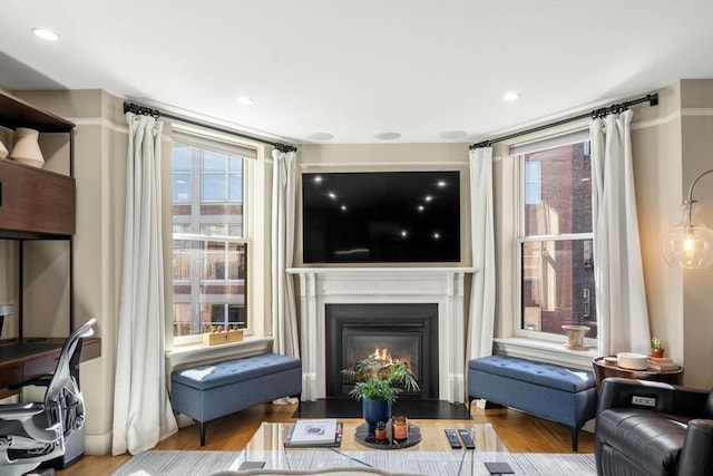 living area with recessed lighting, a fireplace with flush hearth, and wood finished floors