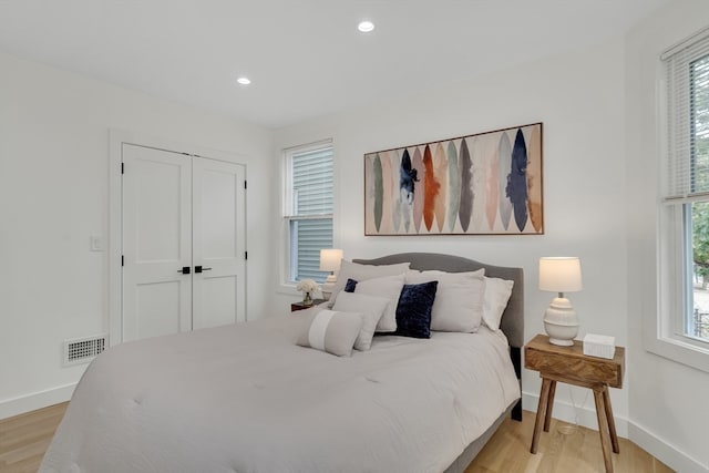 bedroom featuring light wood-type flooring, a closet, and multiple windows