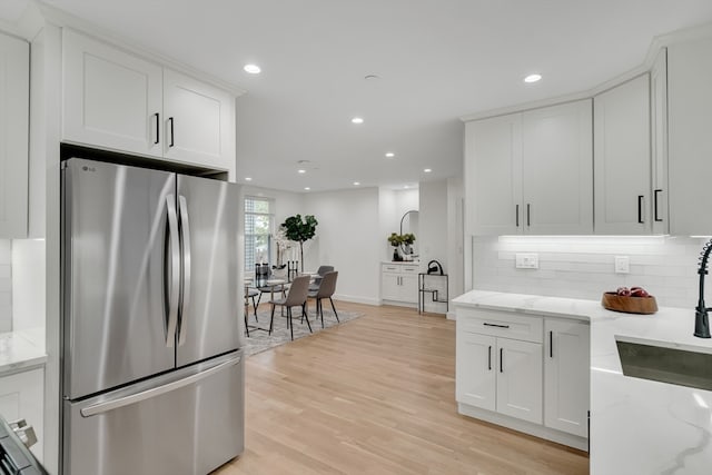 kitchen featuring light wood-type flooring, white cabinetry, stainless steel refrigerator, backsplash, and light stone countertops