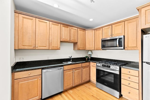 kitchen featuring sink, light hardwood / wood-style floors, dark stone counters, and appliances with stainless steel finishes