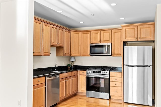 kitchen with appliances with stainless steel finishes, sink, light wood-type flooring, and dark stone counters