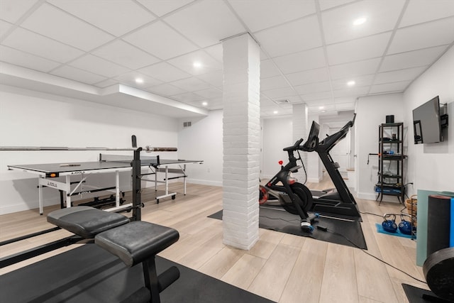 exercise area with decorative columns, light wood-type flooring, and a drop ceiling