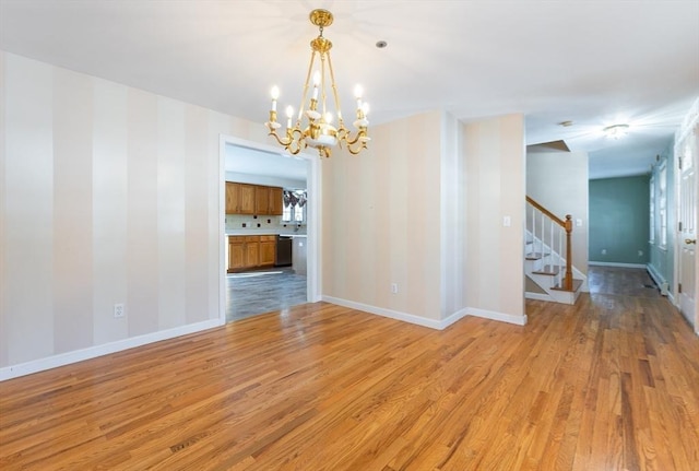 spare room with an inviting chandelier, stairway, light wood-style floors, and baseboards