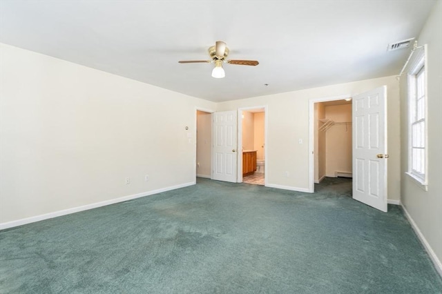 unfurnished bedroom with a walk in closet, baseboards, visible vents, and dark carpet