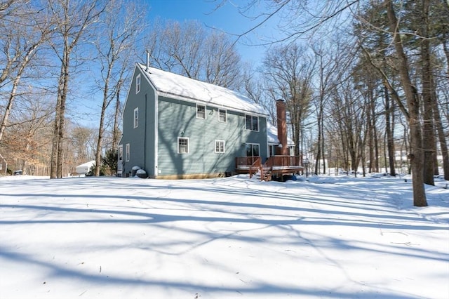 snow covered back of property with a chimney and a wooden deck