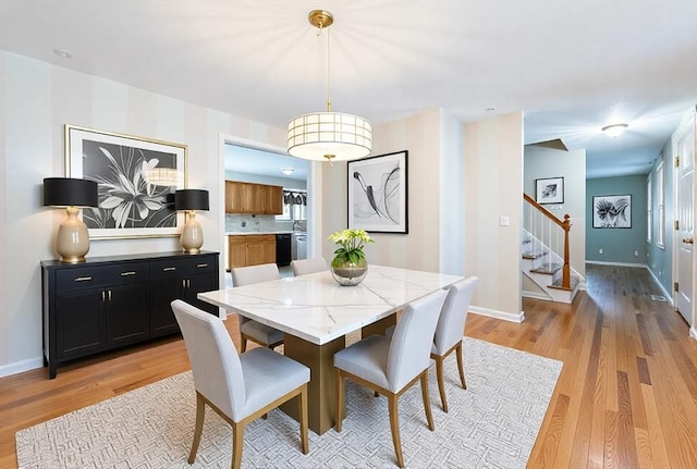 dining room with stairs, light wood-style flooring, and baseboards