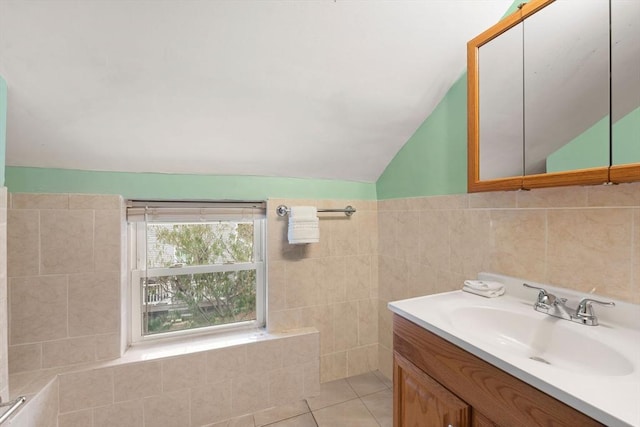 bathroom with lofted ceiling, vanity, tile patterned flooring, and tile walls