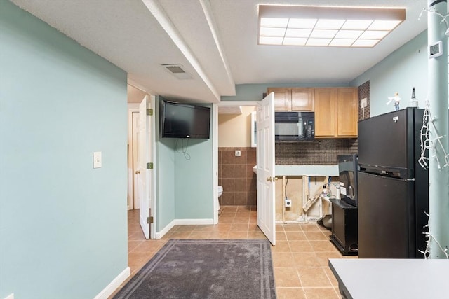 kitchen with light tile patterned flooring, decorative backsplash, light brown cabinets, and black appliances