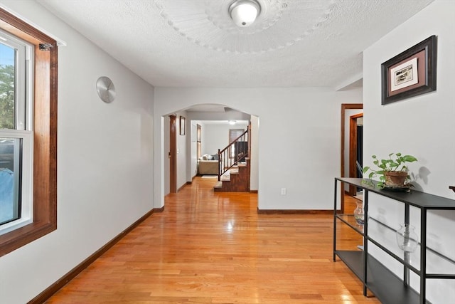 hall with a textured ceiling and light wood-type flooring