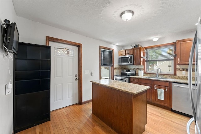 kitchen with appliances with stainless steel finishes, a kitchen island, tasteful backsplash, sink, and light hardwood / wood-style flooring