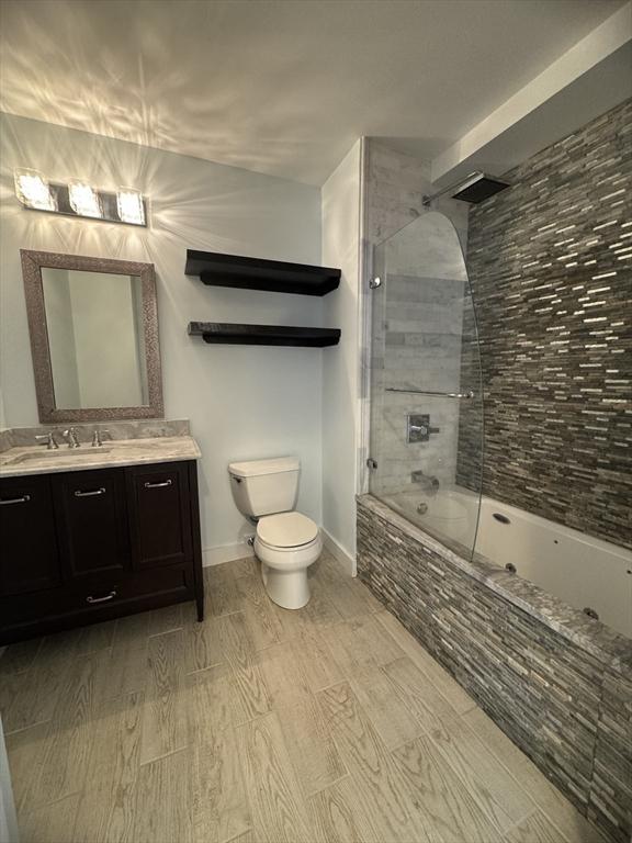 bathroom with toilet, wood finished floors, tiled shower / bath combo, vanity, and baseboards