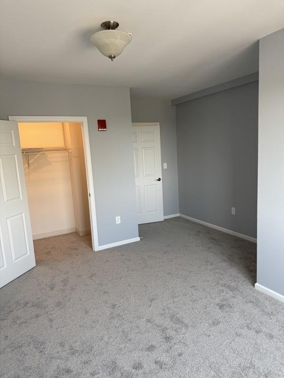 unfurnished bedroom featuring carpet, baseboards, a walk in closet, and a closet