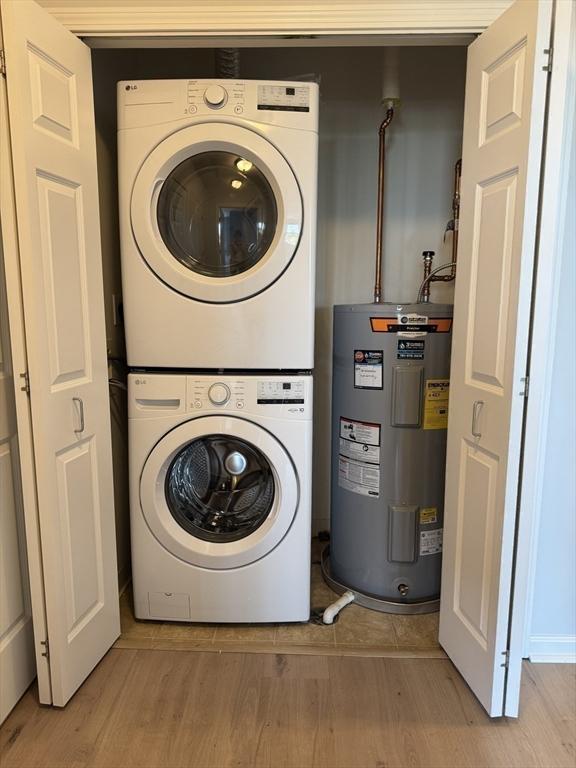 washroom featuring stacked washing machine and dryer, water heater, and light wood-style floors