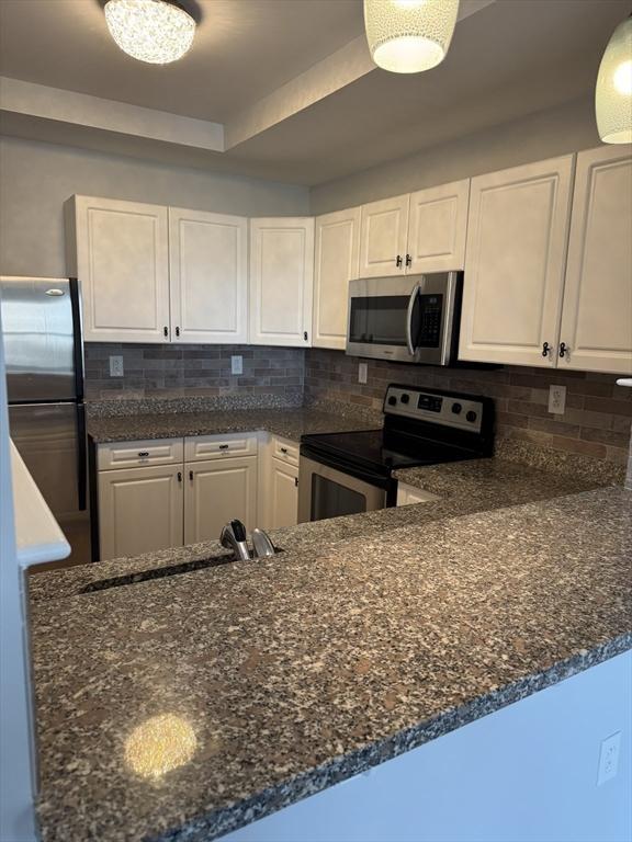 kitchen featuring stainless steel appliances, a sink, white cabinetry, and backsplash