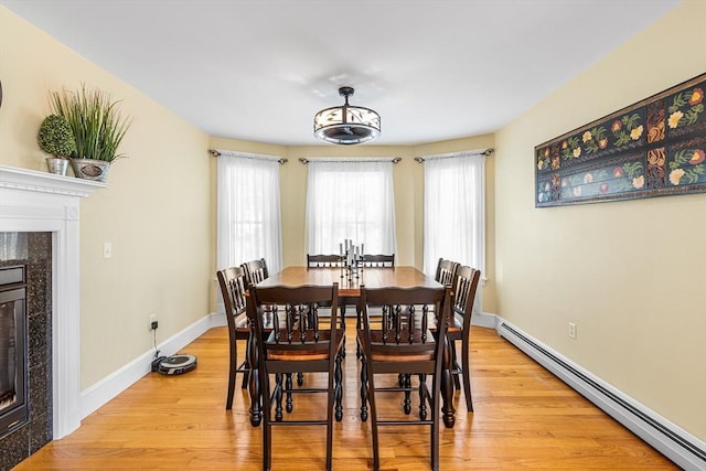 dining space with baseboards, a baseboard radiator, light wood finished floors, and a premium fireplace
