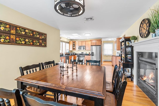 dining area featuring a tiled fireplace, a baseboard radiator, light wood-style flooring, and visible vents