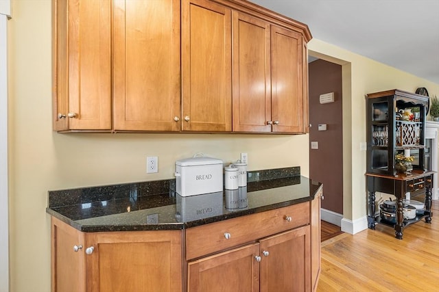 kitchen featuring light wood-style floors, brown cabinets, baseboards, and dark stone countertops