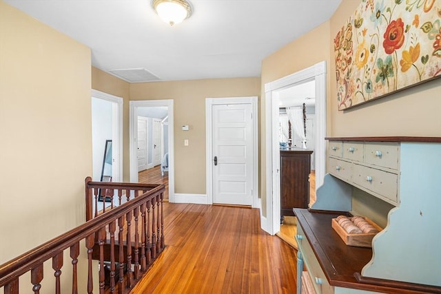 hall with baseboards, visible vents, wood finished floors, and an upstairs landing
