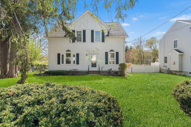 traditional-style house with roof with shingles, fence, cooling unit, a front lawn, and entry steps