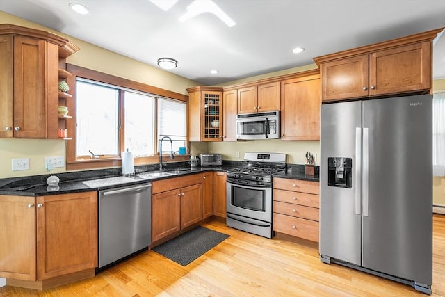 kitchen with appliances with stainless steel finishes, brown cabinets, a sink, dark stone counters, and light wood-style flooring