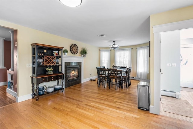 dining space featuring baseboards, light wood finished floors, baseboard heating, and a tile fireplace