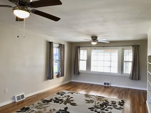 empty room with wood finished floors, baseboards, a ceiling fan, and visible vents