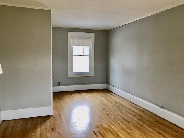 empty room featuring wood finished floors, baseboards, and ornamental molding