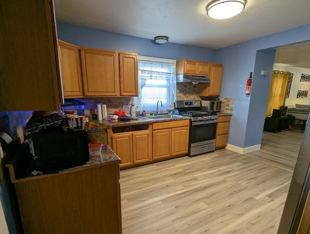 kitchen with backsplash, stainless steel range with gas cooktop, under cabinet range hood, light wood-type flooring, and a sink