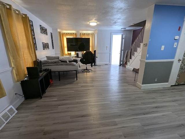 living room featuring visible vents, a textured ceiling, wood finished floors, baseboards, and stairs