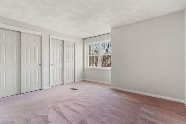 unfurnished bedroom featuring visible vents, two closets, baseboards, carpet, and a textured ceiling