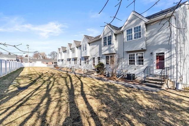 back of property featuring cooling unit, fence, entry steps, a lawn, and a residential view