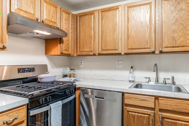 kitchen with under cabinet range hood, appliances with stainless steel finishes, light countertops, and a sink