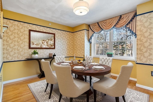 dining space with baseboards, wood finished floors, and wallpapered walls