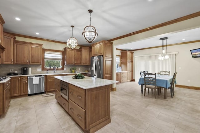 kitchen with sink, appliances with stainless steel finishes, ornamental molding, a kitchen island, and decorative light fixtures