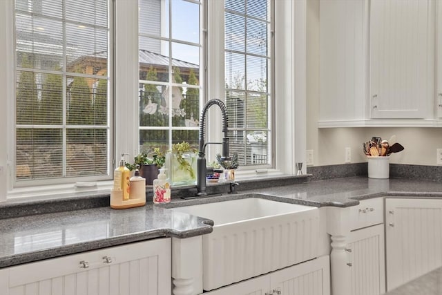 kitchen with white cabinetry, sink, and dark stone counters