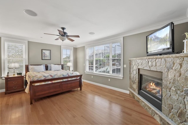 bedroom with ceiling fan, ornamental molding, a stone fireplace, and light hardwood / wood-style floors