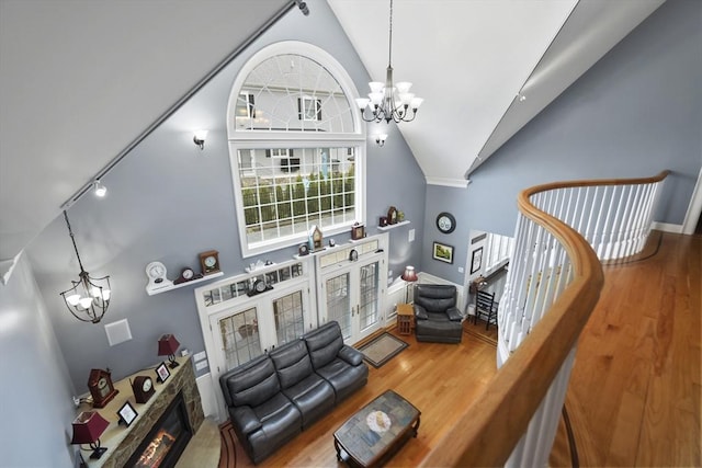 living room featuring hardwood / wood-style floors, high vaulted ceiling, a fireplace, a chandelier, and french doors