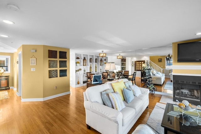 living room featuring light wood-type flooring, an inviting chandelier, and built in features