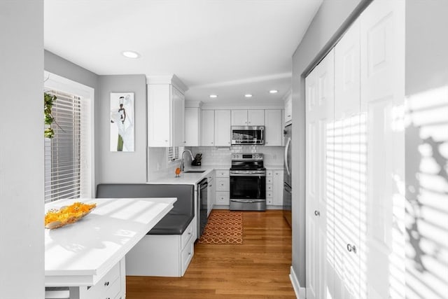 kitchen with appliances with stainless steel finishes, light wood-type flooring, tasteful backsplash, sink, and white cabinetry