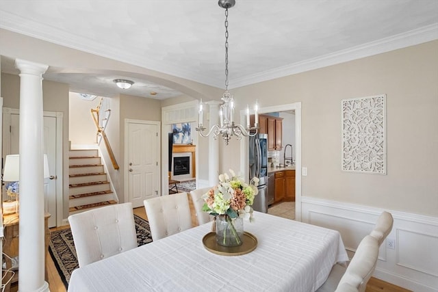 dining room with ornamental molding, stairs, wainscoting, ornate columns, and arched walkways