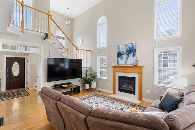 living area featuring a high ceiling, light wood finished floors, baseboards, visible vents, and stairway