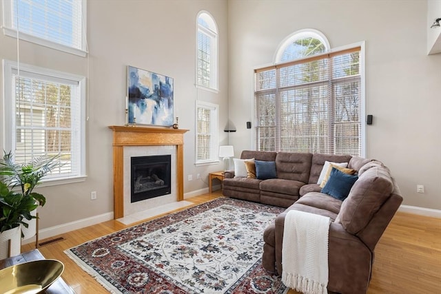 living area featuring visible vents, a towering ceiling, a fireplace, baseboards, and light wood-style flooring