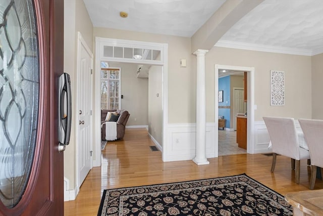 foyer entrance with ornate columns, wainscoting, and light wood finished floors