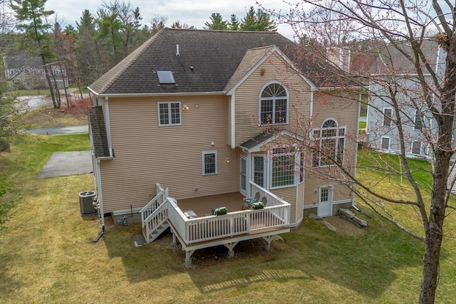 rear view of property with a lawn, a deck, central AC, and roof with shingles
