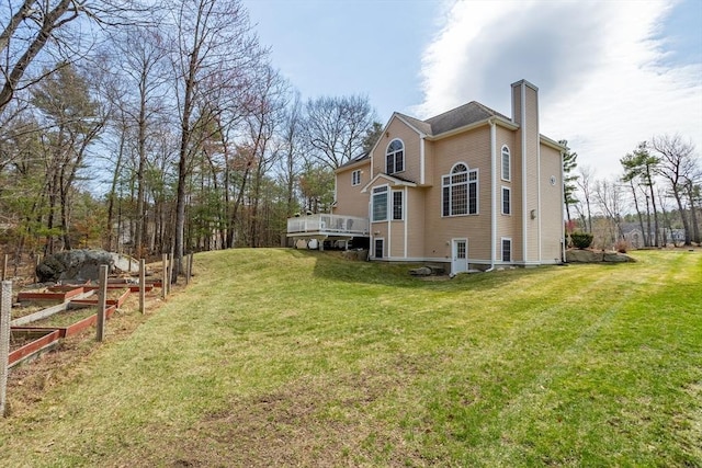 back of house with a lawn, a wooden deck, a chimney, and a garden