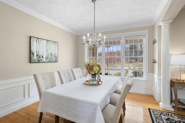 dining space featuring crown molding, wainscoting, light wood-style floors, a chandelier, and ornate columns