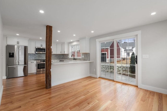 kitchen with sink, white cabinets, light hardwood / wood-style floors, kitchen peninsula, and appliances with stainless steel finishes