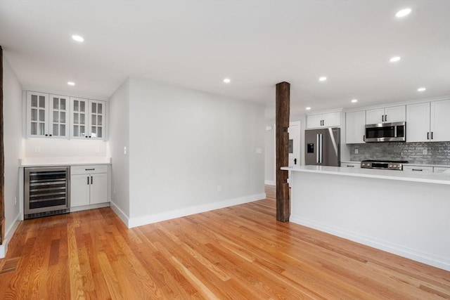 kitchen with stainless steel appliances, beverage cooler, light hardwood / wood-style floors, and white cabinetry