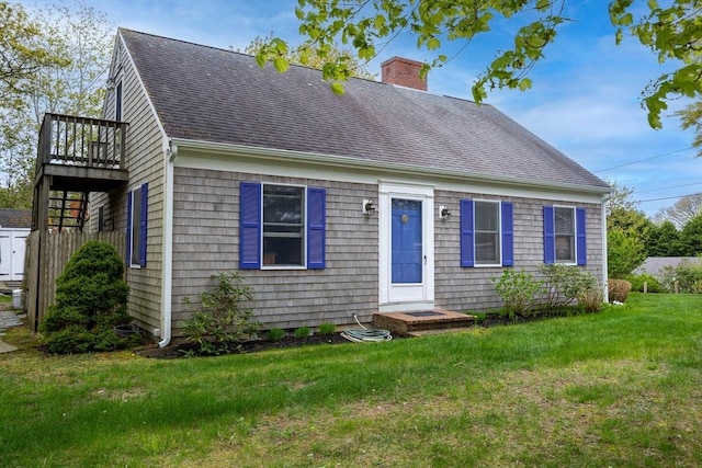 cape cod home with roof with shingles, a front yard, a chimney, and a wooden deck